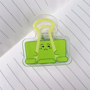 Dettaglio della clip in acrilico verde con emoji triste su carta puntinata per appunti