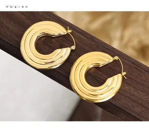 Macro detail of gold textured hoop earrings with multi-layer ripple design on wooden stand