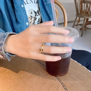Close-up of a minimalist golden adjustable open ring on index finger holding a coffee cup