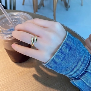 Close-up of minimalist adjustable gold waterdrop ring worn on finger with casual coffee cup