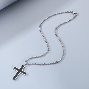 Close-up of a silver cross pendant with black matte texture on a steel chain