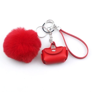 Close-up of red pom-pom keychain with leather mini bag charm and silver metal hardware