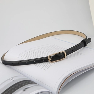 Minimalist black slim leather belt with a golden rectangular buckle on an open book page