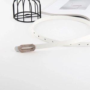 White patent leather skinny belt with golden rhinestone buckle against minimalist props