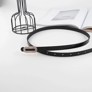 Detail of a thin black patent leather belt with a square rhinestone buckle on a white desk