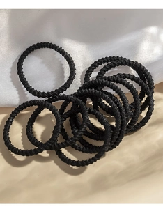 Close-up of small black elastic hair ties with woven texture on beige surface