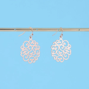 Detail of rose gold hollow mandala earrings hanging on a metallic display stand