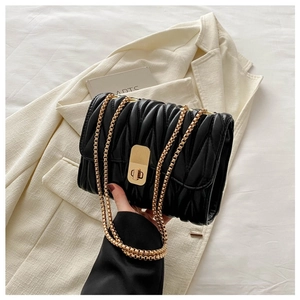 Detail of black quilted leather texture with gold chain strap and metal turn-lock closure