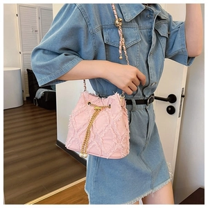 Pink denim bucket bag with gold chain strap and pearl drawstring on a denim dress