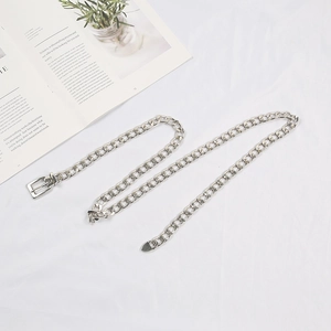 Flat lay of a stylish silver metal chain belt for jeans on a soft white fabric background