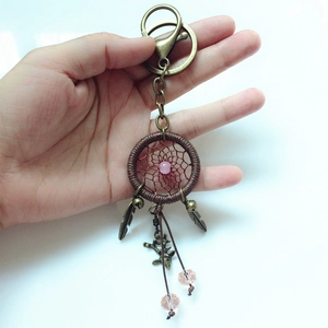 Detail of a handmade dreamcatcher keychain featuring feathers and a pink bead held by hand