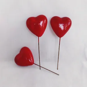 Three red heart foam cake toppers and floral picks on white textured fabric background