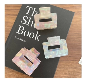 Close-up of three pearlescent square hair claws in pink and blue on a dark book