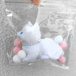 Close-up of white flocked kitten squishy toy with blue necklace in a sealed bag