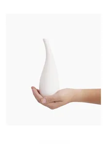 Détail d'une main tenant un vase en céramique blanche au design épuré en goutte