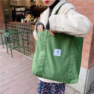 Close-up of green canvas tote bag with a white minimalist patch and wide shoulder strap