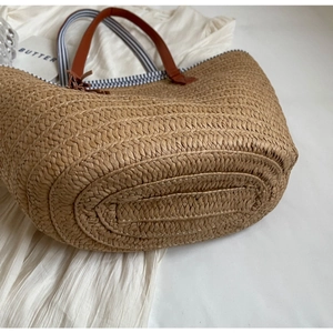Minimalist straw woven tote bag with brown handles and striped lining for beach holidays
