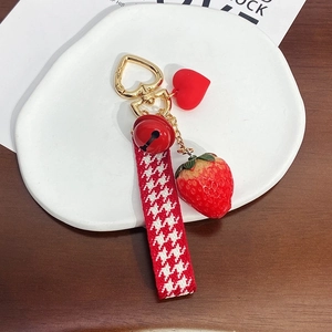 Detail of strawberry keychain with red bell and houndstooth ribbon on a white plate