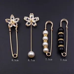 Détail d'un lot de 4 broches décoratives dorées avec strass et perles sur fond gris foncé