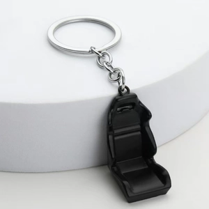 Miniature black racing seat keychain made of metal and plastic on a white pedestal