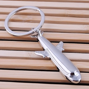 Silver metal airplane keychain fighter jet pendant on a minimalist wooden background