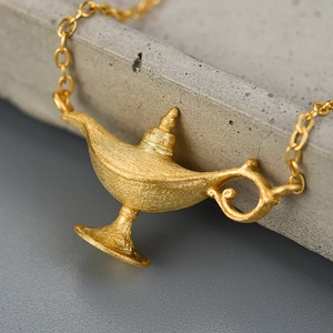 Vintage matte gold Aladdin lamp pendant necklace on a textured grey background