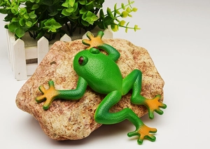 Detailed view of a green and orange toy frog on a rock for realistic garden decoration