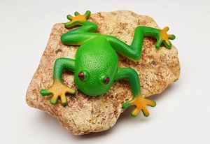 Detailed realistic green frog toy with orange feet resting on a natural stone surface