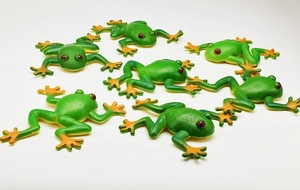 Close-up of eight realistic green and orange toy frogs with red eyes on white background