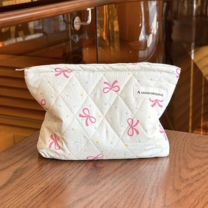 Quilted white cosmetic bag with pink bows and colorful dots on a wooden table