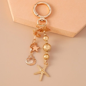 Detailed shot of a golden metal keychain with starfish, seashell, and pearl beads