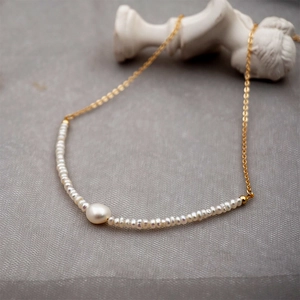 Minimalist freshwater pearl necklace with gold chain draped on a white plaster statue