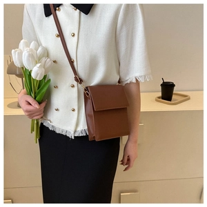 Close-up of a minimalist brown leather crossbody bag styled with a white outfit and flowers