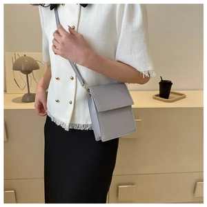 Chic light gray crossbody bag with a sleek flap design shown in a minimalist setting