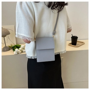 Light grey crossbody mini bag shown on model back view in a minimalist home setting