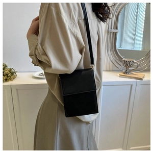 Vertical black crossbody bag in smooth PU leather worn by a model in a minimalist style