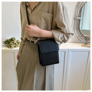 Minimalist black rectangular crossbody bag with leather texture shown in a lifestyle setting