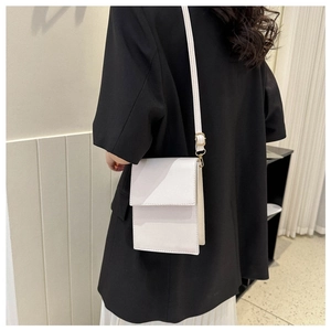 Close-up of a white minimalist rectangle crossbody phone bag worn over a black blazer