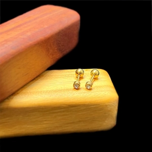 Close-up of gold screw-back stud earrings with white zircons on a wooden texture