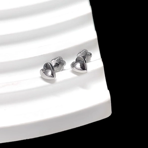 Detail of silver heart-shaped stud earrings on a white minimalist display stand