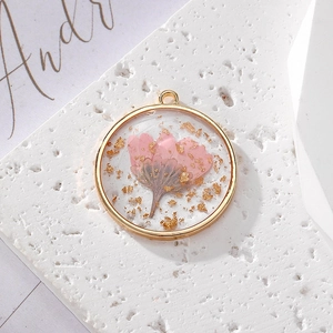 Round resin pendant featuring real pink dried daisy and gold leaf in copper frame