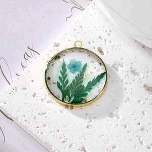 Detailed close-up of a gold metal frame pendant with blue dried flowers and gold leaf