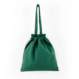 Detail shot of a green canvas drawstring bag with woven beige cords on a white wall