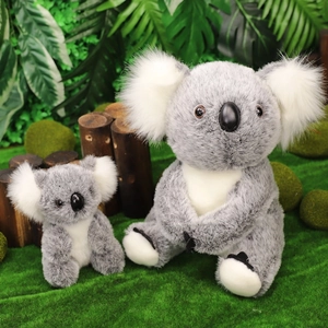Dettaglio di peluche di koala grigi e bianchi su erba naturale e un ceppo di legno