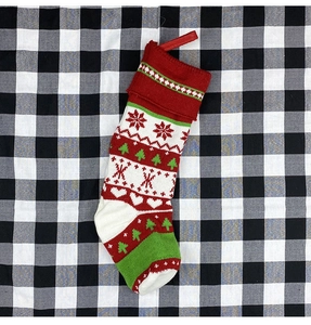 Close-up of knitted Christmas stocking with snowflake and tree patterns on plaid background