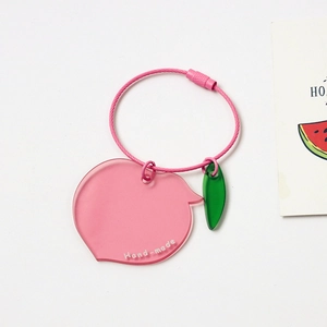 Detail of cute acrylic peach keychain with pink wire loop and hand-made engraving charm