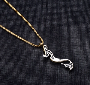 Close-up of gold titanium mermaid pendant necklace on dark textured fabric background