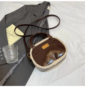 Detail of a brown leather pillow bag with white faux fur trim and gold metal logo plate