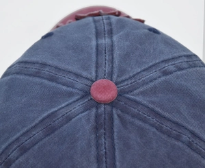 Detailed close-up showing the blue washed cotton fabric and red top button of the cap