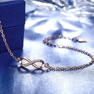 Elegant rose gold infinity bracelet with white zircon stones on a silk blue background